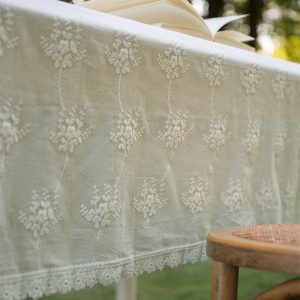 White cotton tablecloth with floral embroidery and lace trim on a rustic table