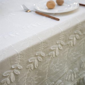 Close-up of delicate green leaf embroidery on white cotton fabric