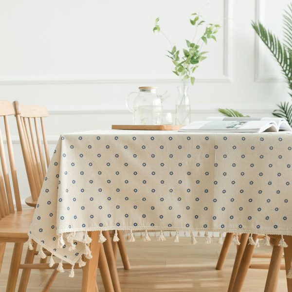 Cotton-linen tablecloth with blue daisy print and tassel trim styled on a rustic dining table.