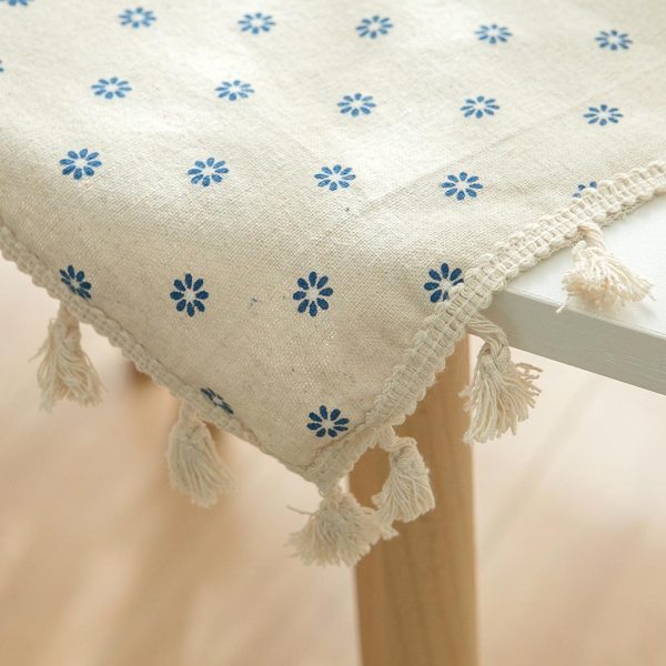 Cotton-linen tablecloth with blue daisy print and tassel trim styled on a rustic dining table.