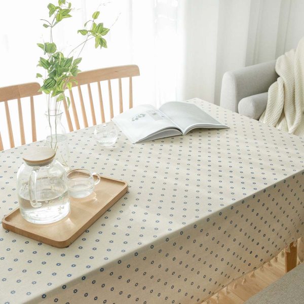 Cotton-linen tablecloth with blue daisy print and tassel trim styled on a rustic dining table.