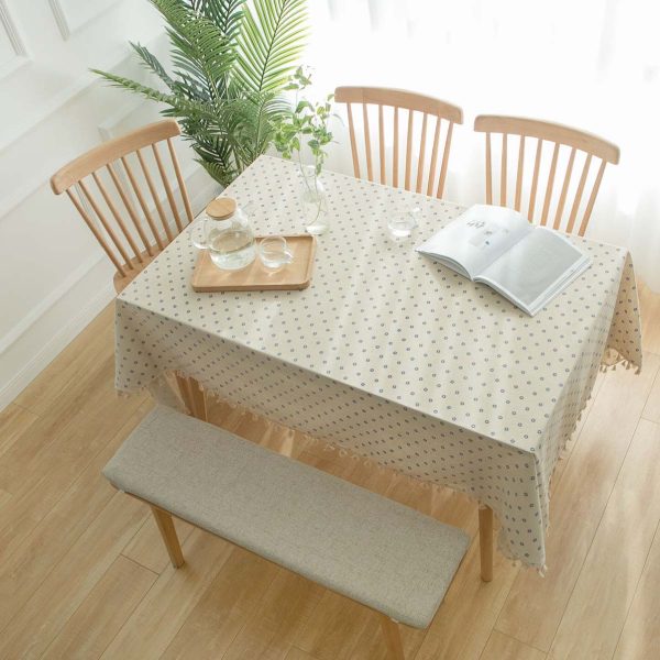 Cotton-linen tablecloth with blue daisy print and tassel trim styled on a rustic dining table.