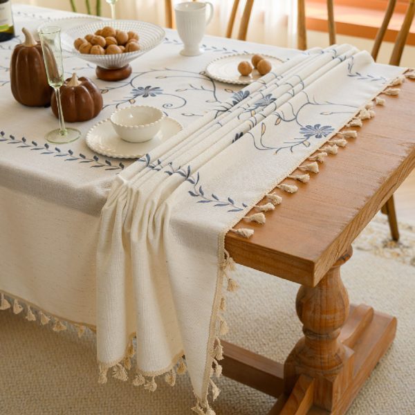 Beige polyester tablecloth with blue floral embroidery and tassel fringe, styled on a farmhouse dining table
