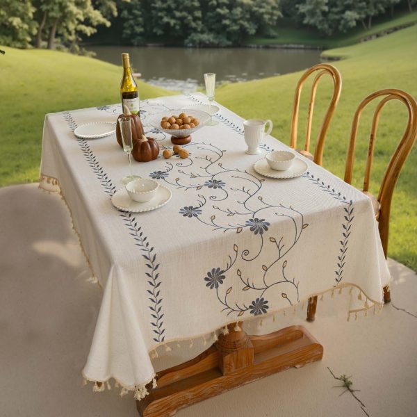 Beige polyester tablecloth with blue floral embroidery and tassel fringe, styled on a farmhouse dining table