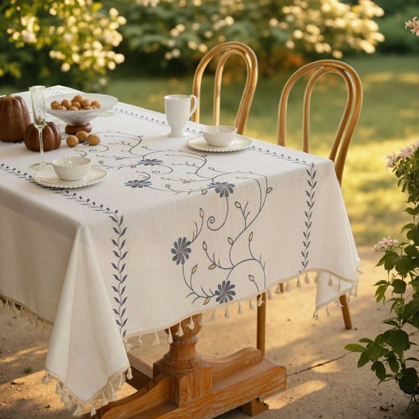 Beige polyester tablecloth with blue floral embroidery and tassel fringe, styled on a farmhouse dining table
