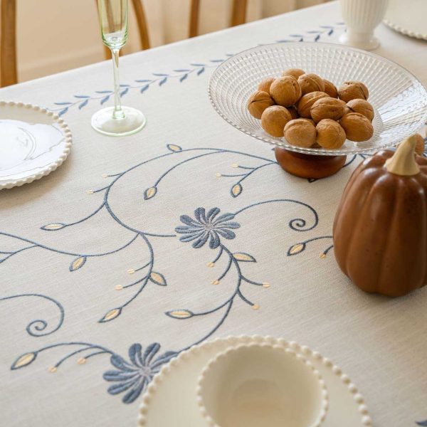 Beige polyester tablecloth with blue floral embroidery and tassel fringe, styled on a farmhouse dining table