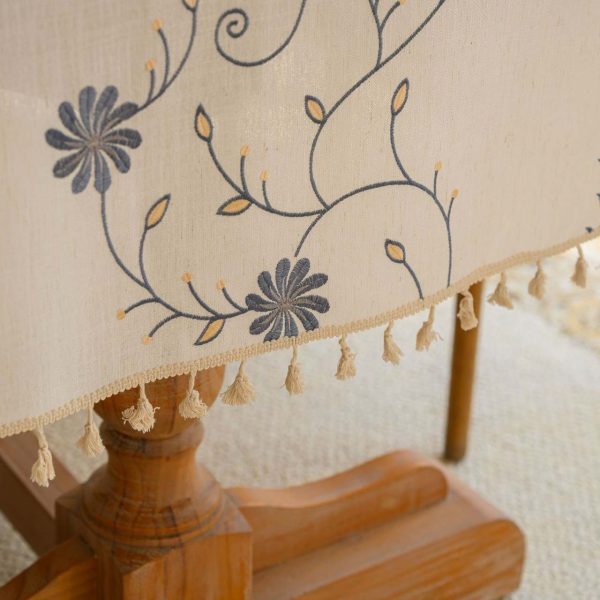 Beige polyester tablecloth with blue floral embroidery and tassel fringe, styled on a farmhouse dining table