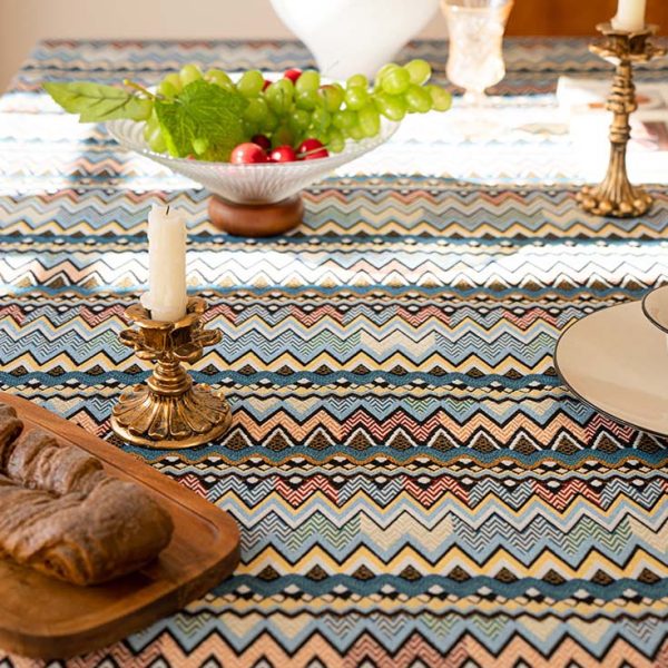 Colorful boho cotton-linen tablecloth with geometric pattern and white tassel trim, styled on a dining table with natural wood chairs.