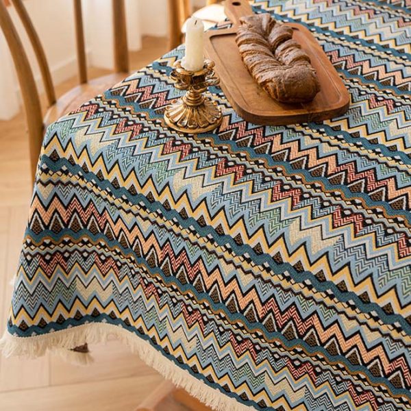 Colorful boho cotton-linen tablecloth with geometric pattern and white tassel trim, styled on a dining table with natural wood chairs.