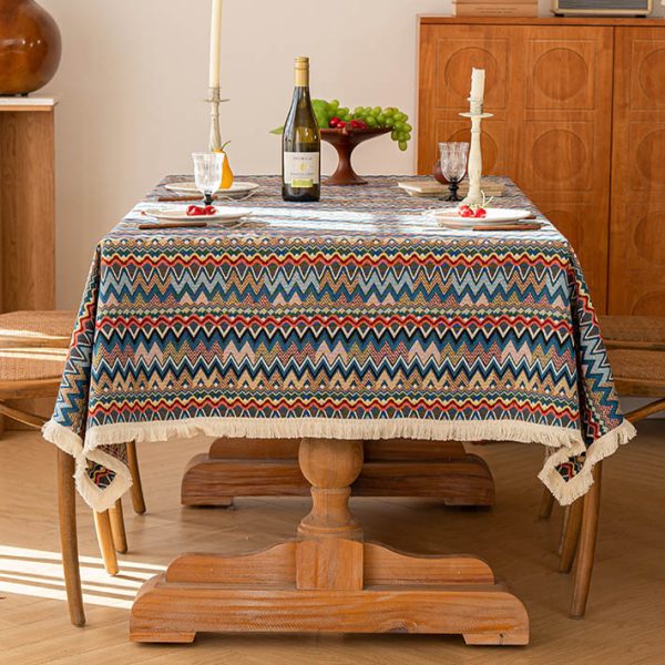 Colorful boho cotton-linen tablecloth with geometric pattern and white tassel trim, styled on a dining table with natural wood chairs.