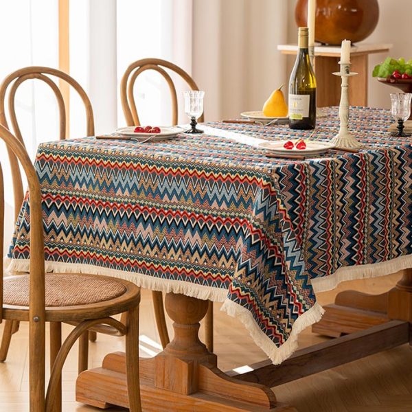Colorful boho cotton-linen tablecloth with geometric pattern and white tassel trim, styled on a dining table with natural wood chairs.
