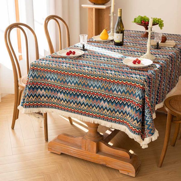 Colorful boho cotton-linen tablecloth with geometric pattern and white tassel trim, styled on a dining table with natural wood chairs.