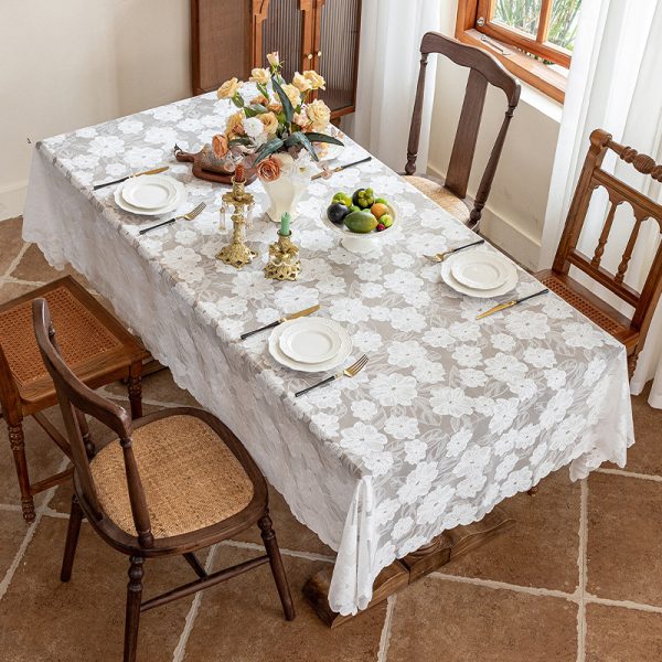 Overhead view of white lace tablecloth with delicate camellia embroidery, styled on a rectangular dining table.