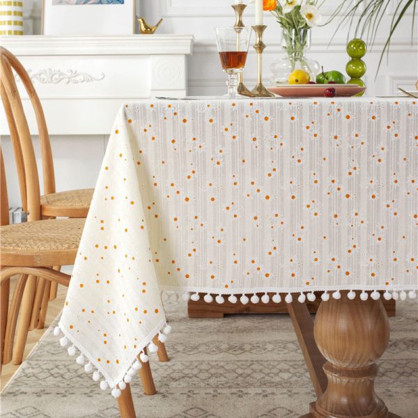 Yellow cotton tablecloth with cheerful daisy print and tassel trim, styled on rustic and outdoor tables for a fresh spring or summer look.