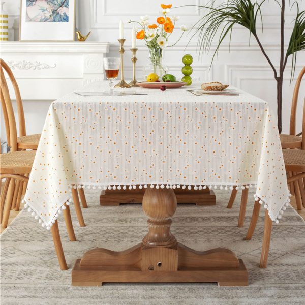 Yellow cotton tablecloth with cheerful daisy print and tassel trim, styled on rustic and outdoor tables for a fresh spring or summer look.