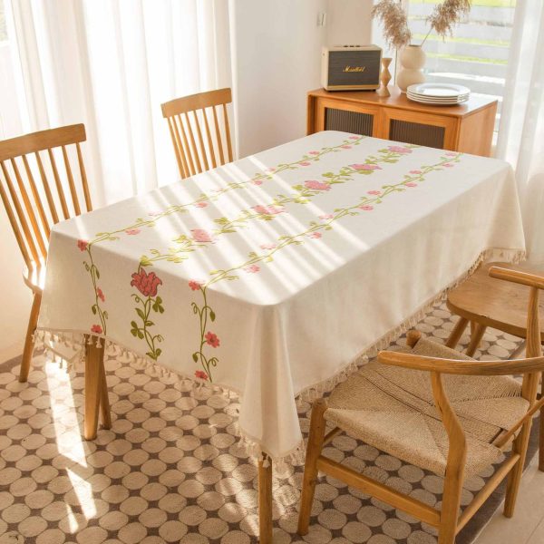 Beige polyester tablecloth with green floral embroidery, draped over a rustic wooden table