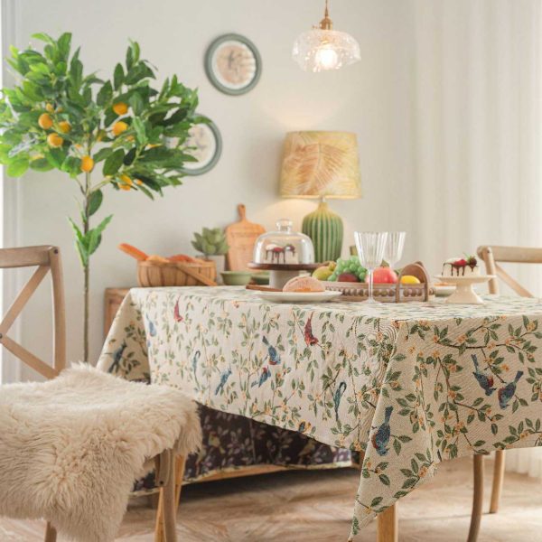 A beige jacquard tablecloth featuring two yellow orioles with green leaves and floral details, adding a touch of rustic charm and elegance to a dining setting.