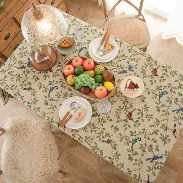 A beige jacquard tablecloth featuring two yellow orioles with green leaves and floral details, adding a touch of rustic charm and elegance to a dining setting.