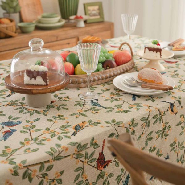 A beige jacquard tablecloth featuring two yellow orioles with green leaves and floral details, adding a touch of rustic charm and elegance to a dining setting.