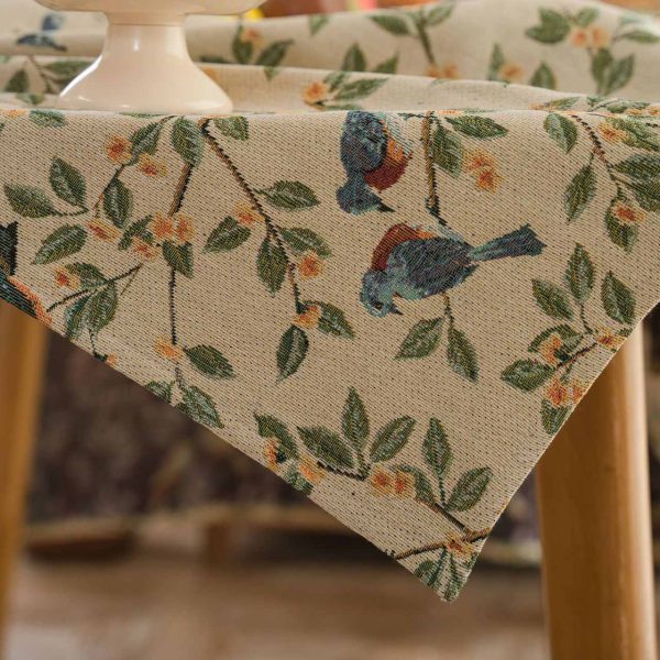A beige jacquard tablecloth featuring two yellow orioles with green leaves and floral details, adding a touch of rustic charm and elegance to a dining setting.