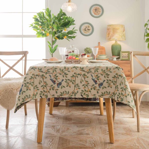 A beige jacquard tablecloth featuring two yellow orioles with green leaves and floral details, adding a touch of rustic charm and elegance to a dining setting.