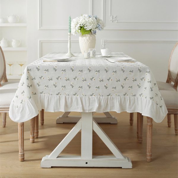 Linen tablecloth with 3D embroidered daisy flowers and ruffled edges, styled on a cozy dining table with wildflowers, creating a soft cottage-style atmosphere.