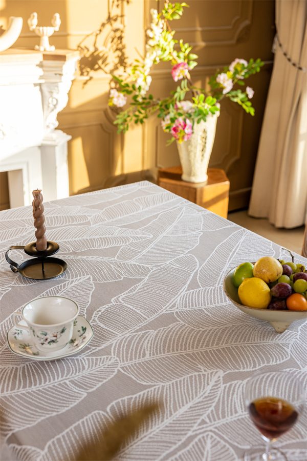 White polyester tablecloth with soft banana leaf print, lace trim, and tassel edge—styled for modern botanical or farmhouse dining.