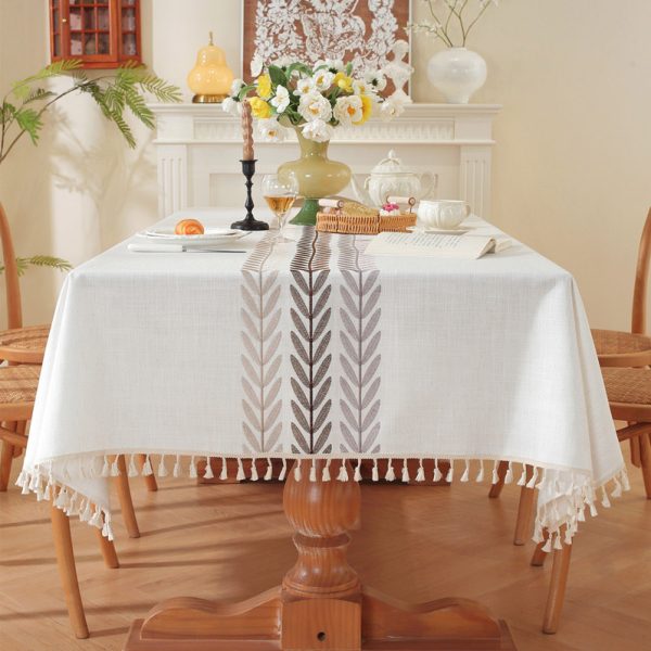 Beige faux linen tablecloth with brown embroidered leaf pattern and tassel fringe, made from polyester-linen blend, suitable for dining tables or outdoor settings.