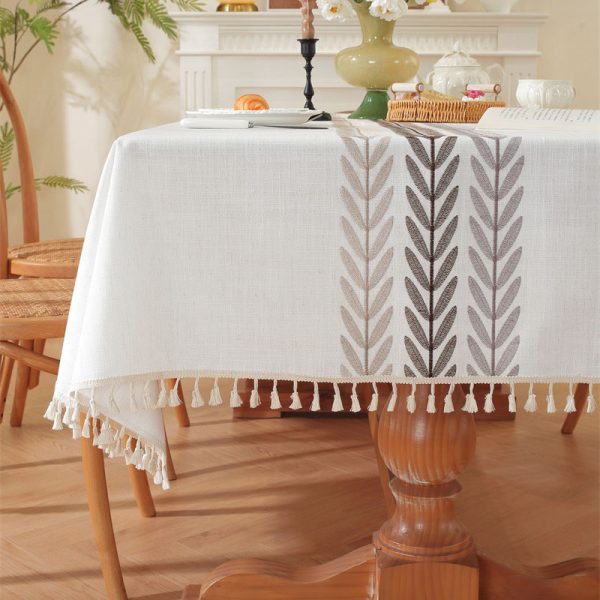 Beige faux linen tablecloth with brown embroidered leaf pattern and tassel fringe, made from polyester-linen blend, suitable for dining tables or outdoor settings.
