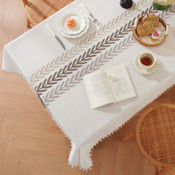 Beige faux linen tablecloth with brown embroidered leaf pattern and tassel fringe, made from polyester-linen blend, suitable for dining tables or outdoor settings.