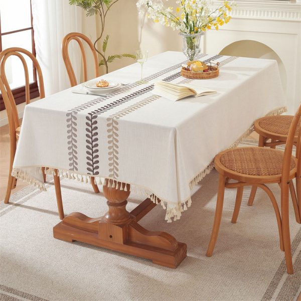Beige faux linen tablecloth with brown embroidered leaf pattern and tassel fringe, made from polyester-linen blend, suitable for dining tables or outdoor settings.