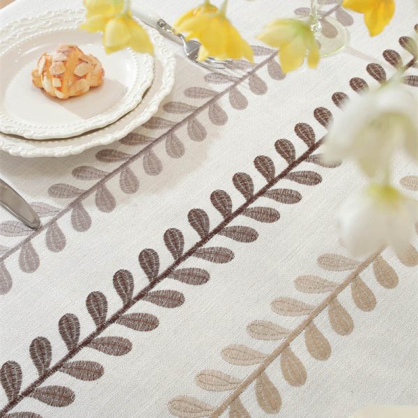 Beige faux linen tablecloth with brown embroidered leaf pattern and tassel fringe, made from polyester-linen blend, suitable for dining tables or outdoor settings.