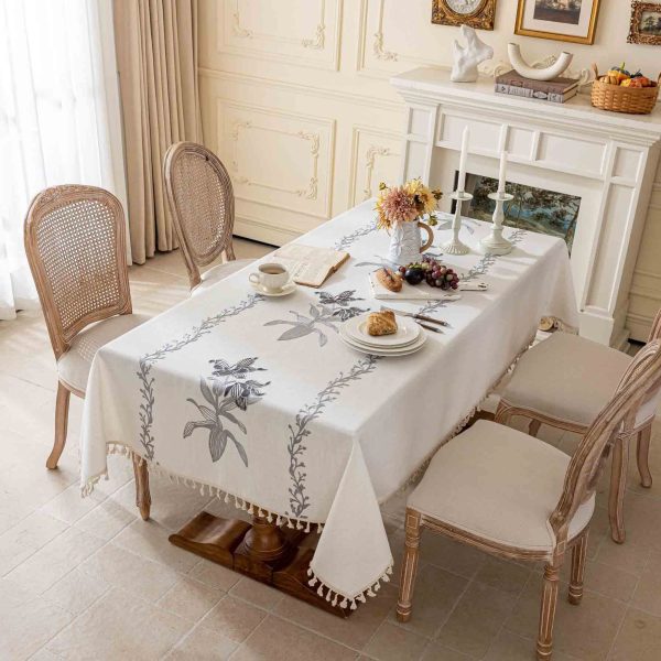 White embroidered tablecloth with gray floral vine pattern on wooden dining table