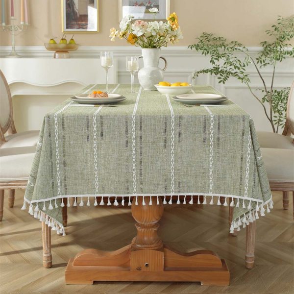 Green polyester tablecloth with white tassel trim and geometric pattern, styled on a dining table for modern home decor