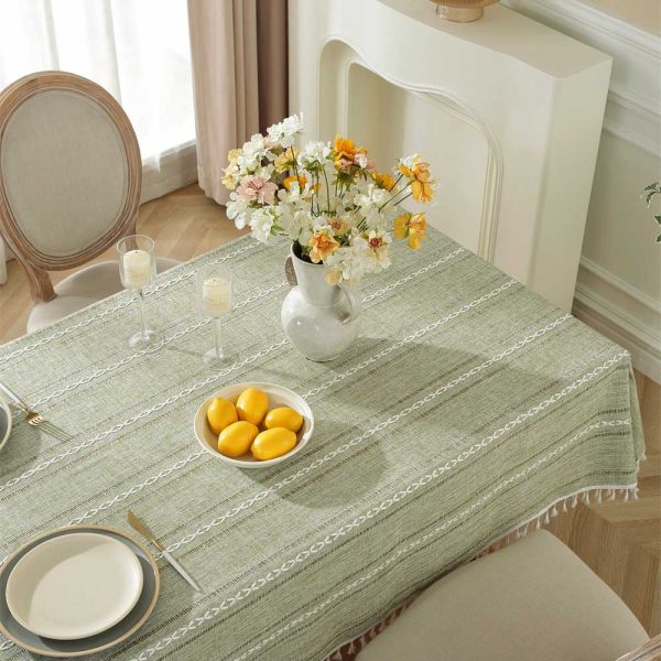 Green polyester tablecloth with white tassel trim and geometric pattern, styled on a dining table for modern home decor
