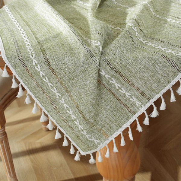 Green polyester tablecloth with white tassel trim and geometric pattern, styled on a dining table for modern home decor