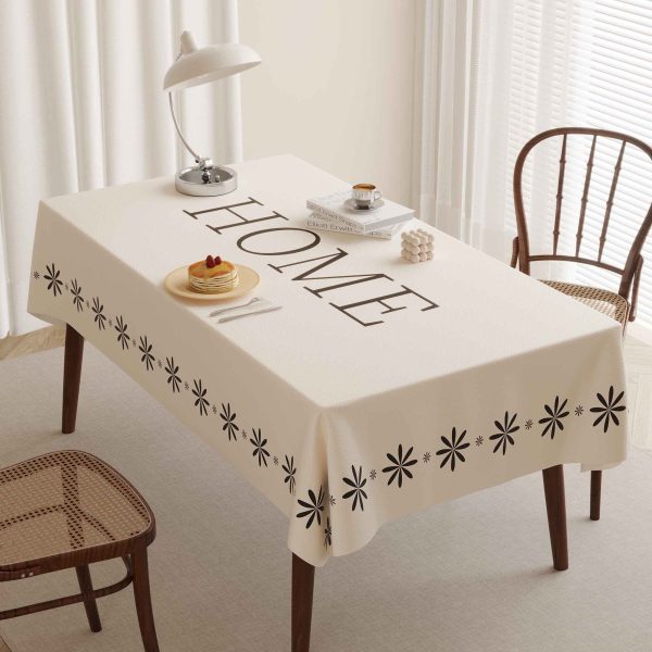 Overhead view of beige waterproof faux leather tablecloth with “HOME” text and floral border on a dining table