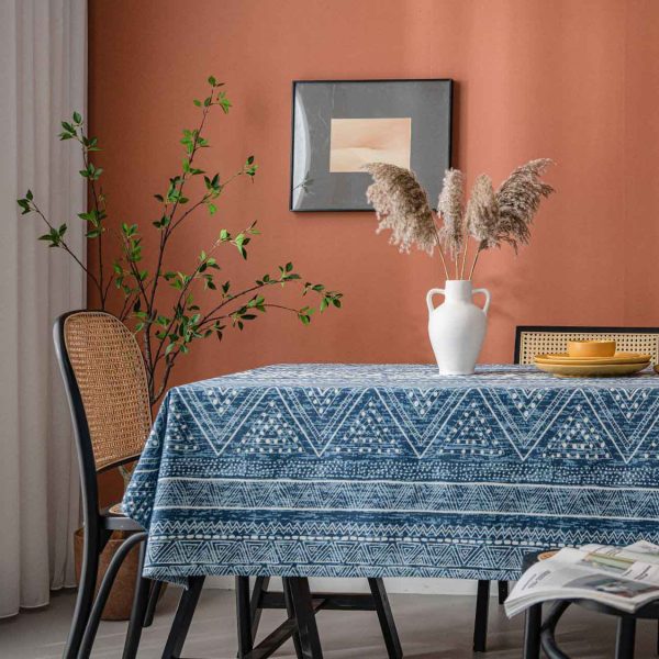 Cotton-linen tablecloth with navy geometric print and tassel trim, styled on a wooden table with white vase and warm-toned wall.