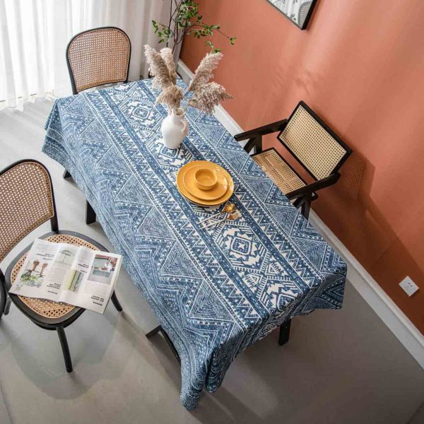 Cotton-linen tablecloth with navy geometric print and tassel trim, styled on a wooden table with white vase and warm-toned wall.