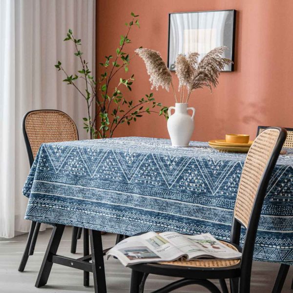 Cotton-linen tablecloth with navy geometric print and tassel trim, styled on a wooden table with white vase and warm-toned wall.