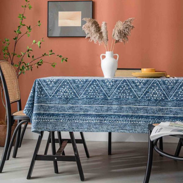 Cotton-linen tablecloth with navy geometric print and tassel trim, styled on a wooden table with white vase and warm-toned wall.