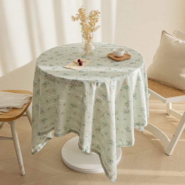 Green lilac floral cotton tablecloth with soft drape on a wood table, styled with glass vase and white teacups.