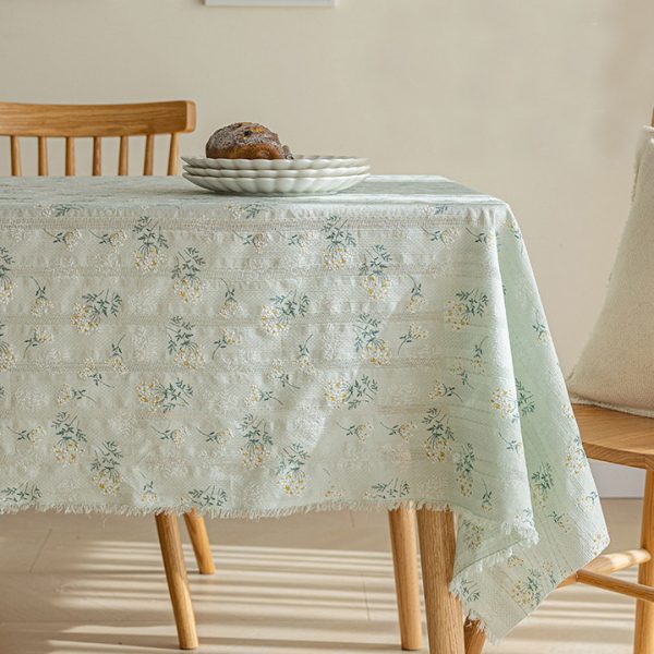 Green lilac floral cotton tablecloth with soft drape on a wood table, styled with glass vase and white teacups.