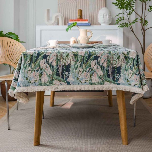 Green lotus floral jacquard tablecloth with white tassel trim, displayed on a dining table in a light-filled kitchen with natural décor.