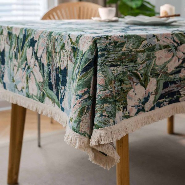 Green lotus floral jacquard tablecloth with white tassel trim, displayed on a dining table in a light-filled kitchen with natural décor.