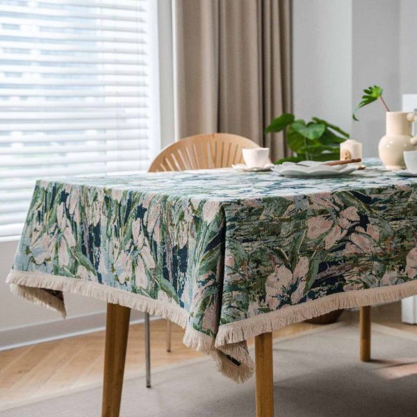 Green lotus floral jacquard tablecloth with white tassel trim, displayed on a dining table in a light-filled kitchen with natural décor.
