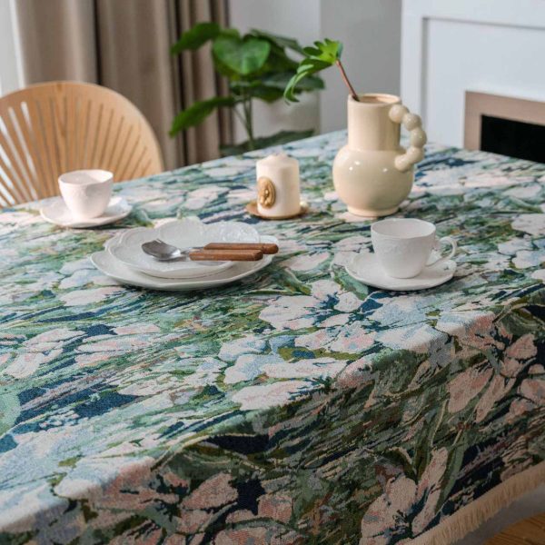 Green lotus floral jacquard tablecloth with white tassel trim, displayed on a dining table in a light-filled kitchen with natural décor.