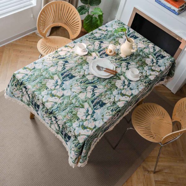Green lotus floral jacquard tablecloth with white tassel trim, displayed on a dining table in a light-filled kitchen with natural décor.