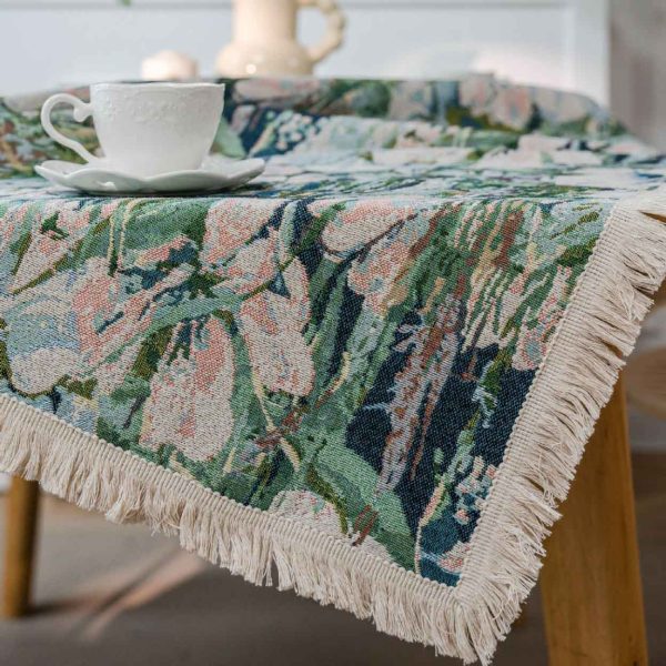 Green lotus floral jacquard tablecloth with white tassel trim, displayed on a dining table in a light-filled kitchen with natural décor.