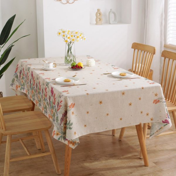Colorful floral polyester-linen tablecloth with vintage botanical pattern on a light background, styled on a rustic dining table with glassware and wooden chairs.